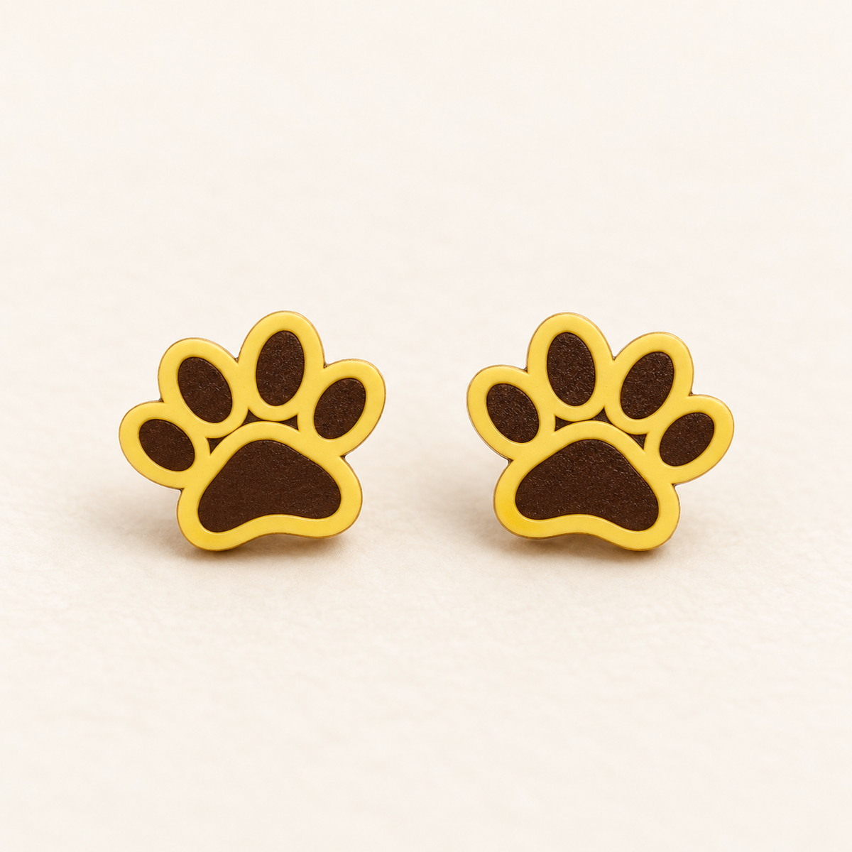 Yellow paw print stud earrings with solid dark brown filled pads, pair on ivory studio background